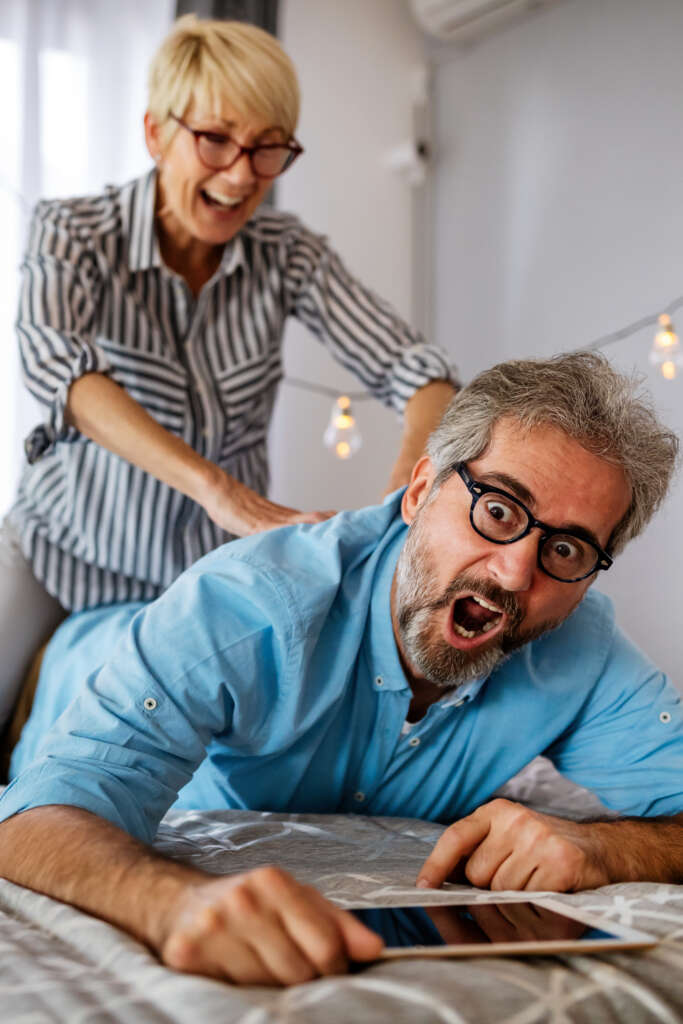 Prone lying man pulls a face as if in pain as hiswife squeezes his back