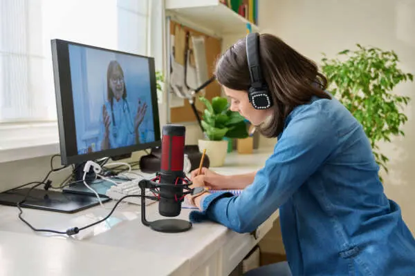 Woman sat at a desk with a microphone and headphones on, talking via a screen to a healthcare professional