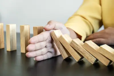 hand stopping falling collapse wooden block dominoes effect from continuous toppled block, falls prevention and development of balance and stability.